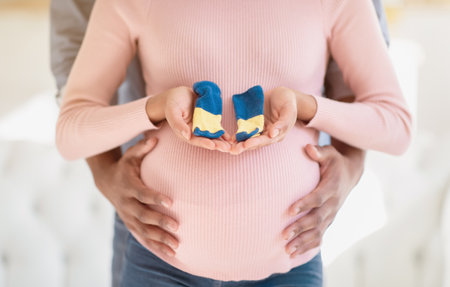 Cropped view of black pregnant woman and her husband with tiny baby socks, closeupの写真素材
