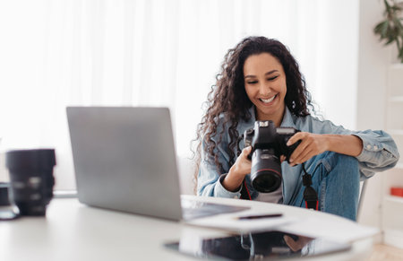 Joyful Professional Photographer Lady Holding Camera Using Laptop At Workplace