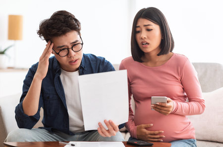 Depressed Japanese Couple Struggling Financial Crisis Looking At Bills Indoorの写真素材