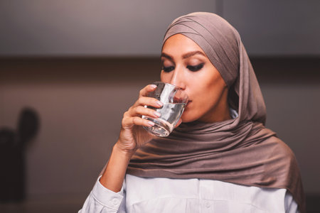 Muslim Lady Drinking Water From Glass In Kitchen At Homeの写真素材