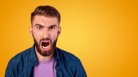 Portrait of young bearded guy shouting furiously, expressing his anger over grey studio background....