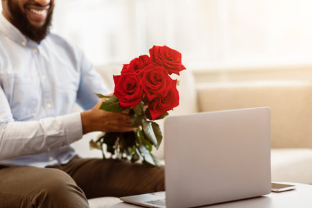 Black man holding red roses, showing to laptop cameraの写真素材