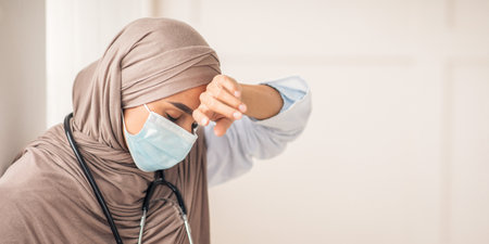 Stressed muslim doctor in face mask touching her foreheadの写真素材