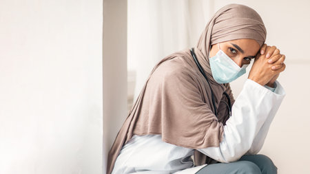 Pensive muslim woman doctor sitting next to wall in hospitalの写真素材