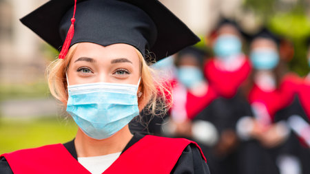 Young blonde lady in graduation costume and face mask, closeupの写真素材