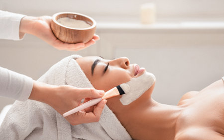 Relaxed asian woman getting facial nourishing mask by beautician at cosmetology cabinetの写真素材