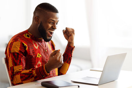 Online Win. Joyful Black Man In Traditional Shirt Celebrating Success With Laptopの写真素材