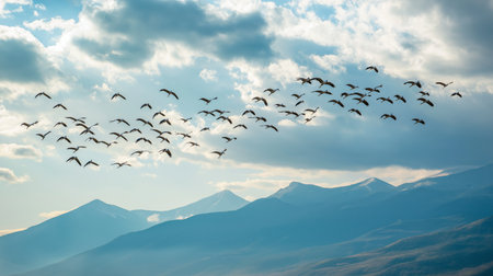 Birds fly gracefully in formation over mountainous terrain as the sun sets in the backgroundの素材