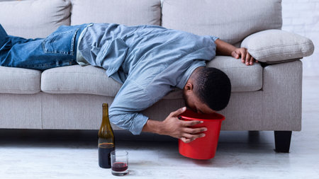 Drunk Man Vomiting Into Bucket After Drinking Wine Lying Indoorの写真素材