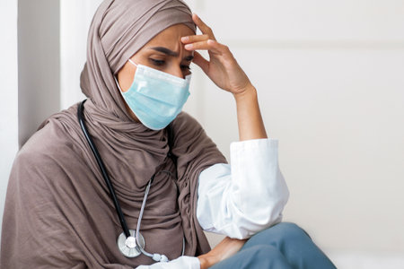 Fatigued physician young woman in hijab resting at her cabinetの写真素材