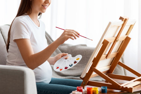 Pregnancy Leisure. Happy pregnant woman painting on easel at homeの写真素材