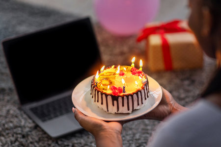 Closeup of black woman holding birthday cake, using laptopの写真素材