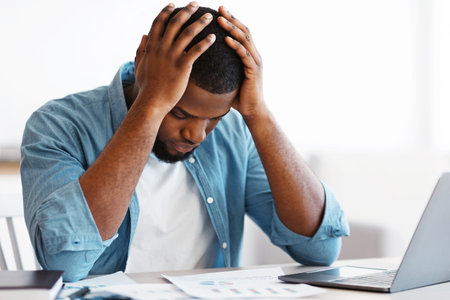 Bankruptcy Concept. Depressed Black Businessman Sitting At Desk With Laptop And Papersの写真素材