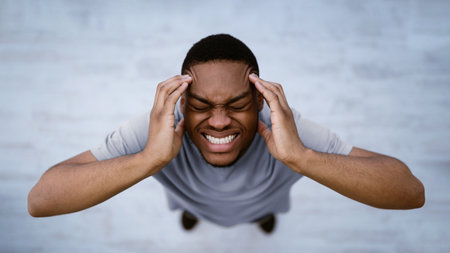 Black Man Having Headache Suffering From Pain Standing Indoors, Top-View