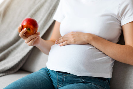 Prenatal Nutrition. Closeup Of Pregnant Lady Holding Red Apple And Embracing Belly