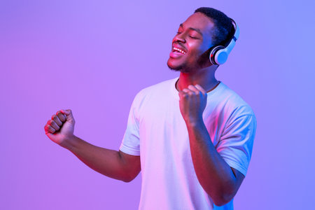 Millennial African Man Wearing Wireless Headphones Listening Music And Singing, Neon Lightの写真素材