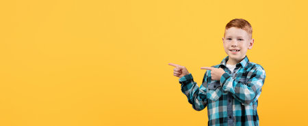 Cute ginger boy pointing at empty space on yellow
