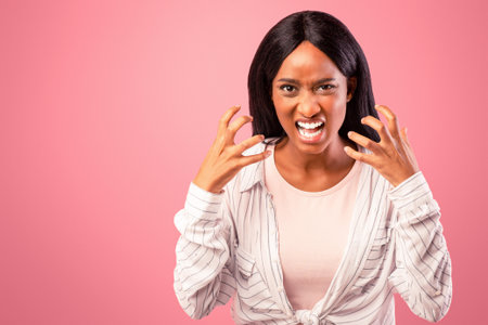 Angry black woman screaming out loud, tired of her problems, expressing negative emotions over pink studio backgroundの写真素材