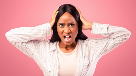 Furious black woman screaming and holding her head on pink studio backgroundの写真素材