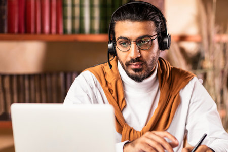 Indian Student Studying Online At Laptop Wearing Headset Sitting Indoor