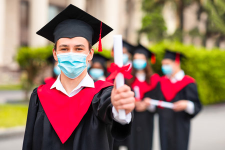 Caucasian guy student in graduation costume showing diplomaの写真素材