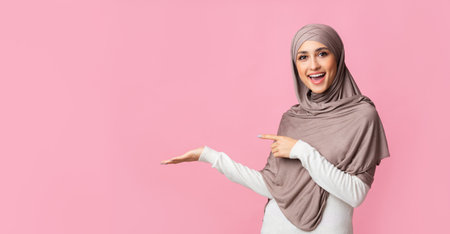 Beautiful girl in hijab pointing at something on her empty palmの写真素材