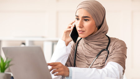 Female doctor looking at laptop screen and talking on phoneの写真素材