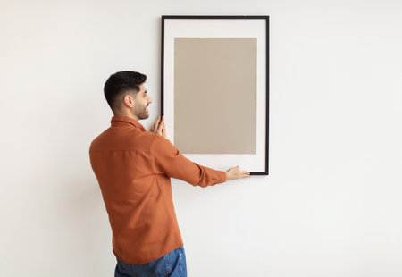 Young man hanging picture frame on the wall
