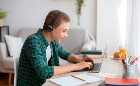 Cheerful schooler with headset typing on laptop