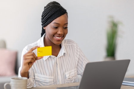 Smiling african woman freelancer holding credit card, working on laptopの写真素材