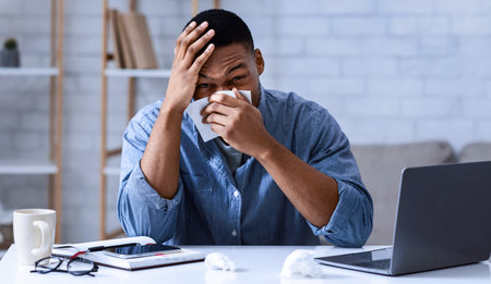 Ill Black Man Blowing Nose In Napkin Sitting In Office