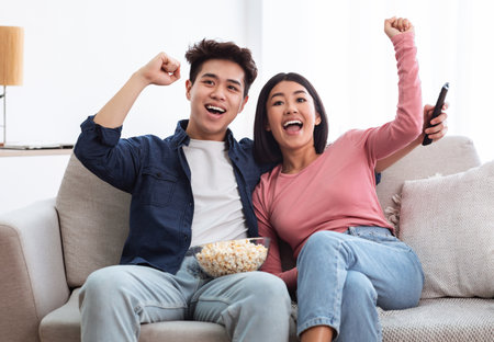 Excited Chinese Couple Watching TV Shaking Fists In Living Room