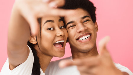 Happy couple looking through finger frame, pink backgroundの写真素材