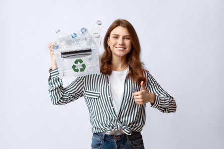 Smiling woman holding recycle bin with plastic bottles and showing thumb up