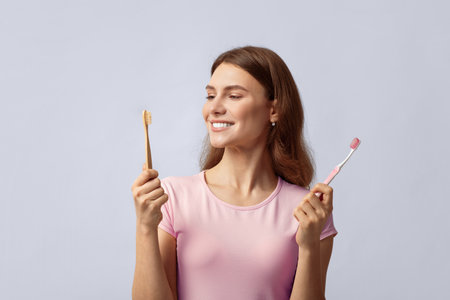 Smiling young woman holding eco bamboo and plastic toothbrushの写真素材