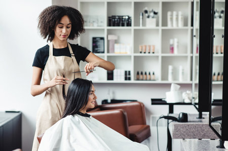 Young woman enjoying haircut at beauty salon with black masterの写真素材