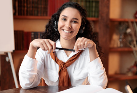 Confident woman in headset posing and sitting at deskの写真素材