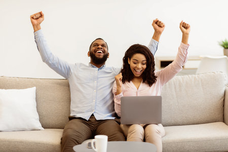 Black couple using laptop celebrating success with clenched fistsの写真素材