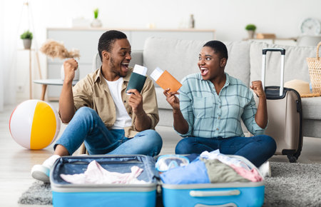 Black Couple Holding Tickets Shaking Fists Celebrating Vacation At Homeの写真素材