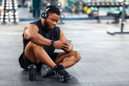 Tired black guy bodybuilder sitting on floor, listening to music