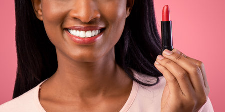 Gorgeous black woman holding tube of lipstick on pink studio backgroundの写真素材