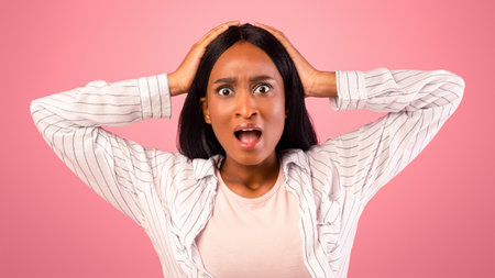 Unbelievable news. Emotional black woman holding her head in shock over pink studio background