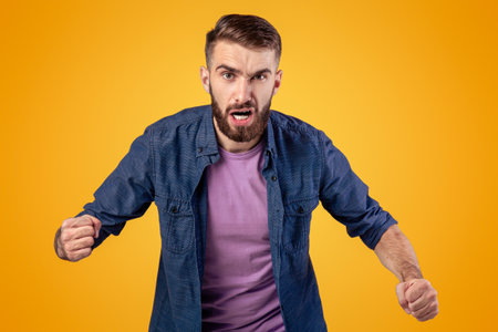 Portrait of young angry man shouting with rage, clenching fists on grey studio backgroundの写真素材