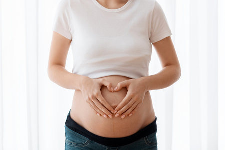 Happy pregnant woman making heart gesture with hands near her naked belly