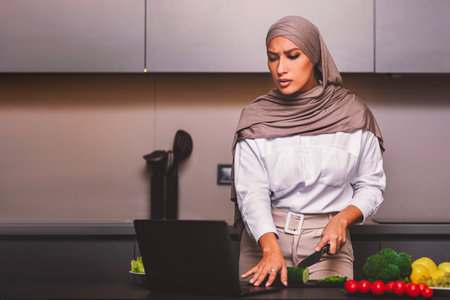 Muslim Woman Learning To Cook Watching Videos On Laptop Indoorの写真素材