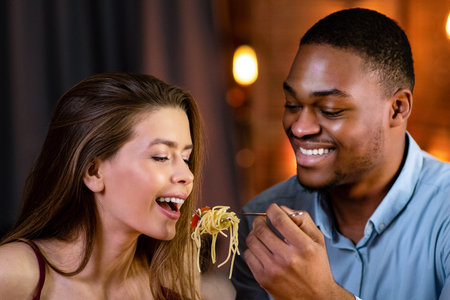 Romantic Interracial Couple Having Fun During Dinner In Restaurant, Eating Spaghetti Together