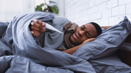Sick Black Guy Measuring Temperature Having Fever In Bed Indoors