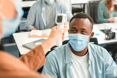 Teacher with contactless thermometer gun measuring temperature of black studentの写真素材