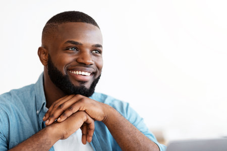 Successful African American freelancer guy sitting at desk with laptop looking asideの写真素材