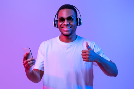 Black Man In Headphones Holding Smartphone And Showing Thumb Up, Neon Lightingの写真素材
